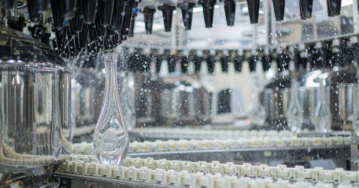 Clear glass perfume bottles passing through an automated washing and drying tunnel with air knives in a glass factory