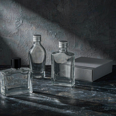 Empty clear glass cologne bottles in masculine shapes with black and metal caps arranged on dark stone, unfilled and unlabelled