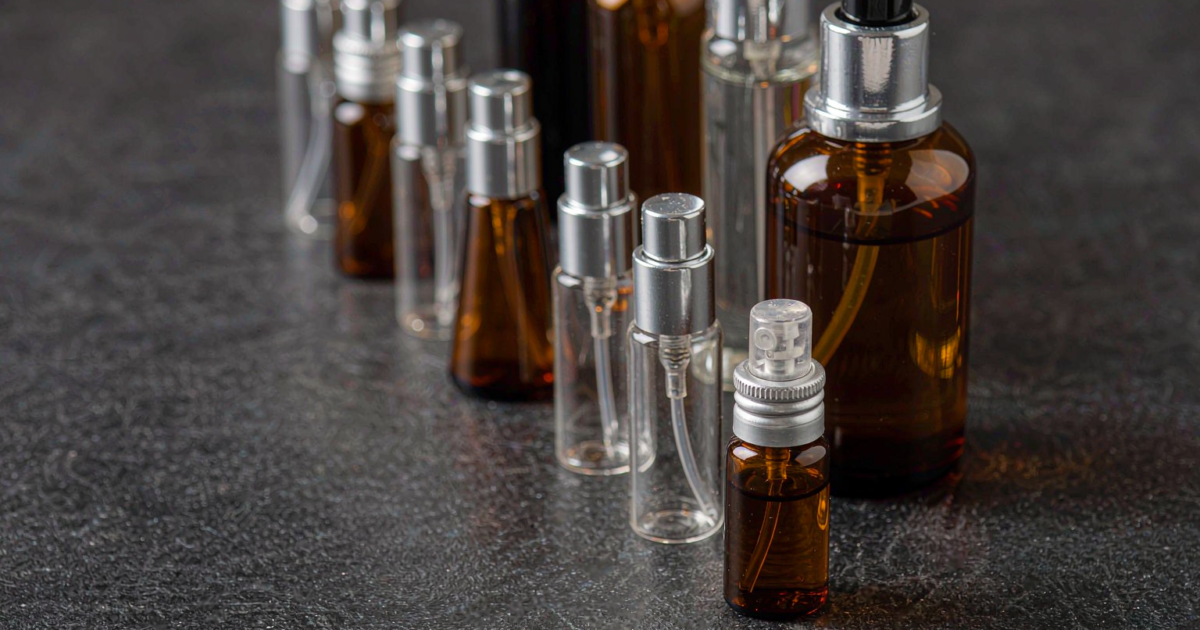 A collection of small 5ml to 15ml glass perfume bottles and travel sprays lined up on a dark stone surface under soft studio lighting