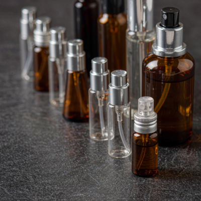 A collection of small 5ml to 15ml glass perfume bottles and travel sprays lined up on a dark stone surface under soft studio lighting