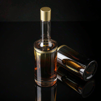 A sleek refillable glass perfume bottle with amber gradient and minimal gold cap on a reflective dark surface, next to a refill pouch