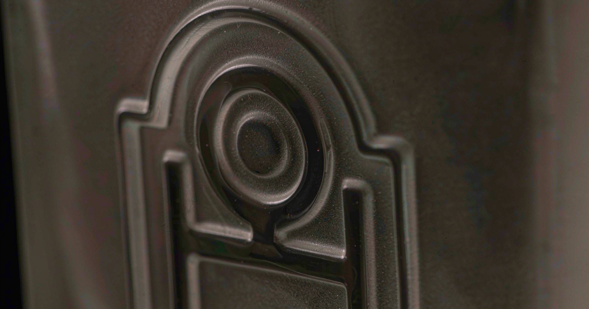 Macro view of a raised 3D embossed emblem pressed into frosted perfume bottle glass under raking light