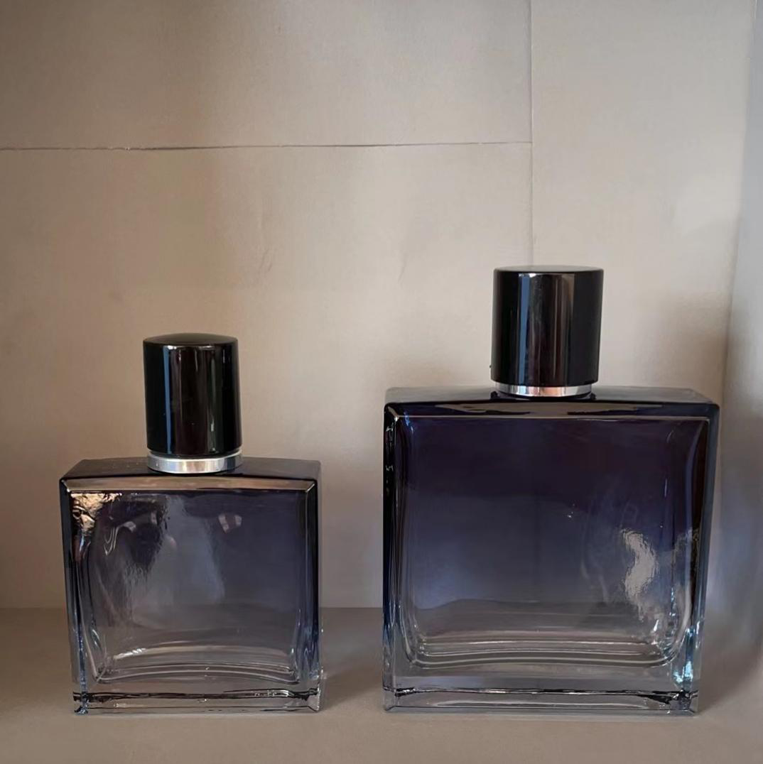 Clear glass perfume bottle with rectangular flask body, thick heavy base, plated collar and glossy black cylindrical overcap, two sizes shown
